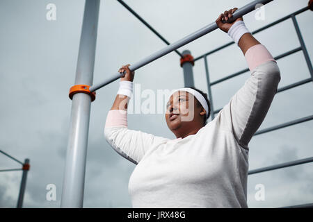 Determined overweight African woman practicing pull-up exercise outdoors Stock Photo