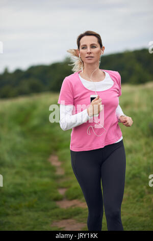 Concentrated woman listening to music running through field, copy space to the left Stock Photo