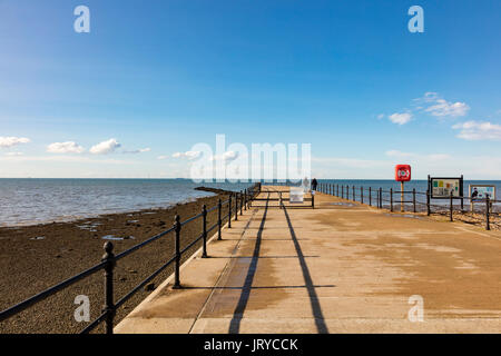 An elderly couple walk along Hampton Pier in the low evening light,, against a blue sky, Herne Bay, Kent, UK Stock Photo