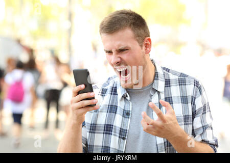 Angry man holding crashed mobile phone on the street Stock Photo