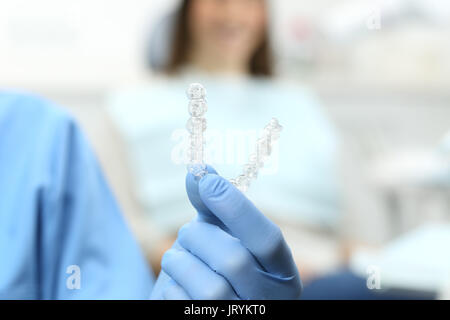 Dentist hand with gloves holding a silicone trainer in a consultation with a patient in the background Stock Photo