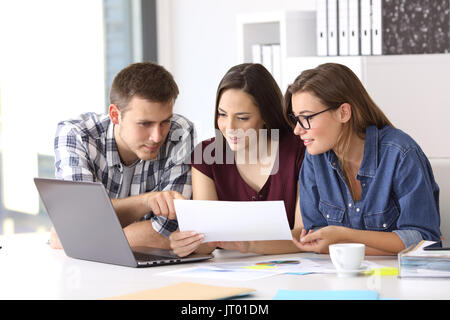 Three coworkers working at office comparing data with laptop and documents Stock Photo