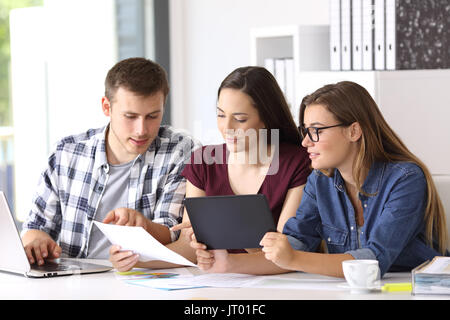 Three employees coworking on line with multiple devices at office Stock Photo