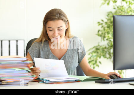 Front view of a happy employee reading reports sitting in a desktop at office Stock Photo