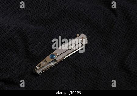 Knife with a metal handle in folded form on black textiles. Iron on black. Stock Photo