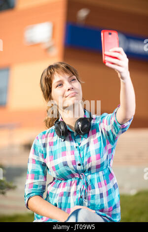 Happy young girl taking pictures of herself through cell phone, over collage campus. Selfie woman. Stock Photo