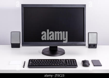 Black blank pc monitor stay on desk, around ordered space to work with keyboard, computer mouse, smartphone, speakers, pen and sticky notes. Stock Photo