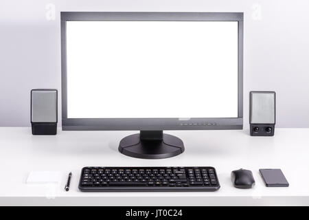 White blank pc monitor stay on desk, around ordered space to work with keyboard, computer mouse, smartphone, speakers, pen and sticky notes. Stock Photo