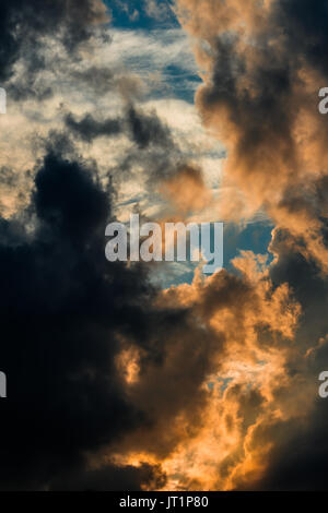 Bright Orange and Dark Grey Clouds against Patches of Blue Sky. A Golden Pathway of Light is Created by the Glow of the Setting Sun. Stock Photo