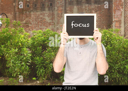 Portrait of handsome young man holding chalkboard with text 'focus'. Business concept. Outdoors. Stock Photo