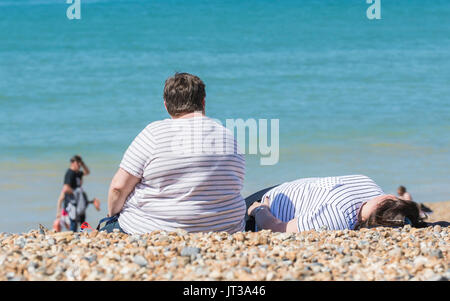 Overweight woman sitting on a beach. Large lady sat in the sun on a beach in the UK. Obese person on a beach. Stock Photo