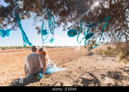 Newlywed couple sitting under shade of tree in summer Stock Photo