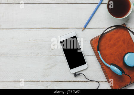 Top view / Flat Lay the pen / note book / white mobile phone / listening radio music by headphones / black coffee and eyeglasses on rustic table woode Stock Photo