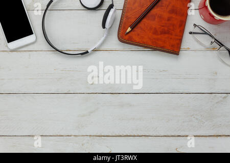 Top view / Flat Lay the pen / note book / white mobile phone / listening radio music by headphones / black coffee and eyeglasses on rustic table woode Stock Photo