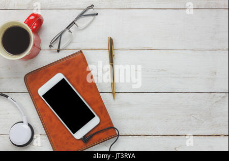 Top view / Flat Lay the pen / note book / white mobile phone / listening radio music by headphones / black coffee and eyeglasses on rustic table woode Stock Photo