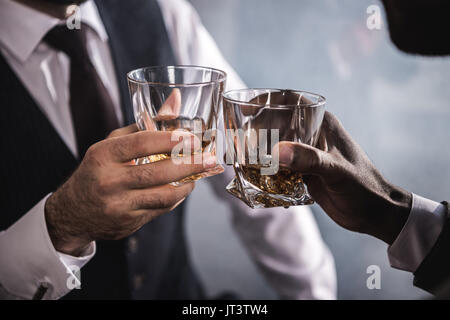 Close-up partial view of two men in formal wear clinking whiskey glasses Stock Photo