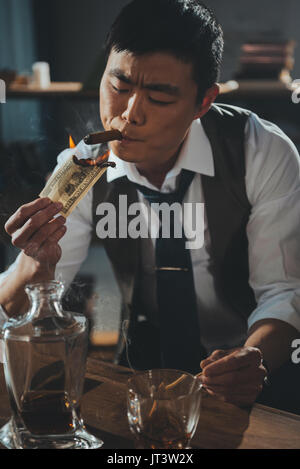 confident asian businessman smoking cigar and burning dollar banknote  Stock Photo