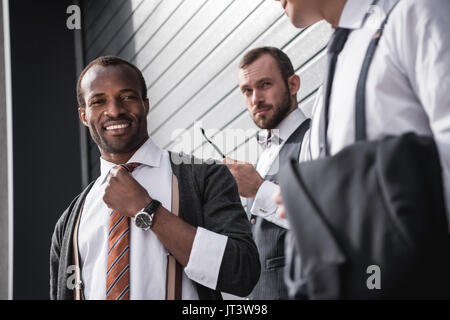 young stylish multiethnic businessmen in formalwear standing outdoors, business team meeting Stock Photo