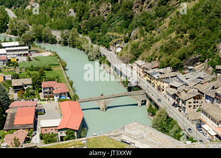 Roman stone bridge crosses Dora river at medieval mountain village, shot from above on a bright summer day at Bard valley, Aosta,  Italy Stock Photo