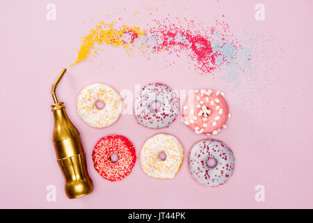 Top view of variety frosted donuts and golden bottle on pink surface. donuts chocolate background Stock Photo