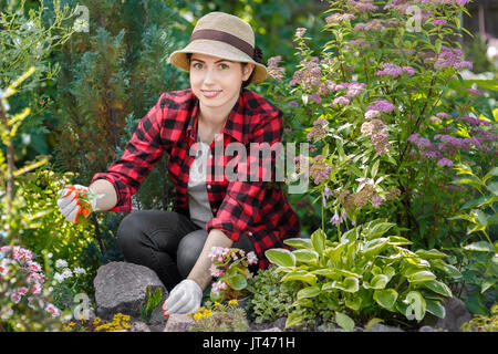 young woman gardener care of flowers in the garden. Girl pulling out the weeds in flowerbed. People, gardening, care of flowers, hobby concept Stock Photo