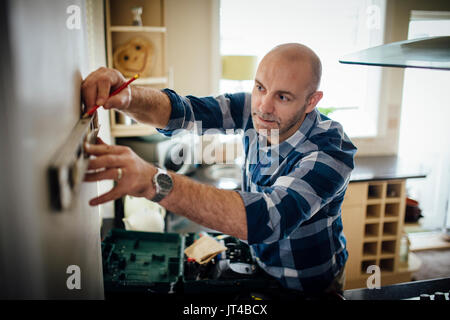 Mature man using a spirit level and marking the wall with a pencil in his kitchen. Stock Photo