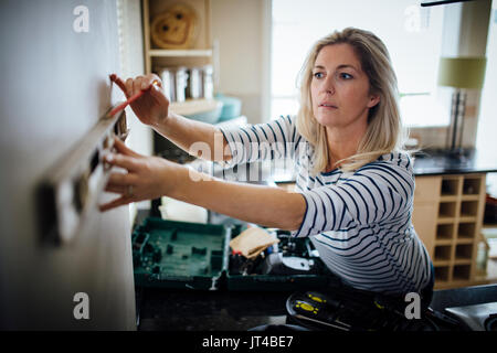 Mature woman using a spirit level and marking the wall with a pencil in her kitchen. Stock Photo