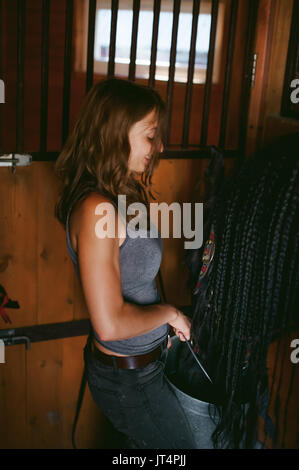 female horseman holding a bucket of water quenching thirst  Friesian horse, in a stable on a farm, caring for thoroughbred pets Stock Photo