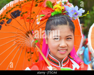 Pretty Thai Chinese girl in traditional dress with orange parasol smiles for the camera. Stock Photo