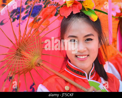 Pretty Thai Chinese Girl in traditional dress with red parasol smiles for the camera. Stock Photo