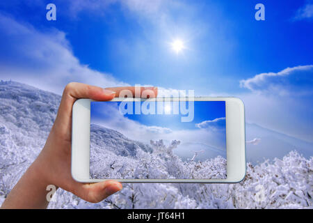 Hand holding smart phone take a photo at Deogyusan mountains in winter. Stock Photo