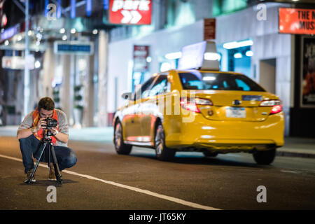 NEW YORK, USA - October 14, 2016. Photographer in the Street of New York taking a long Exposure Picture of Time Square at Night with a Long Zoom Lens Stock Photo