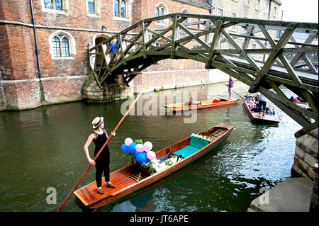 A newly married couple take a river punt in Cambridge passing under the famous mathematical bridge at Queen's College, part of Cambridge University.