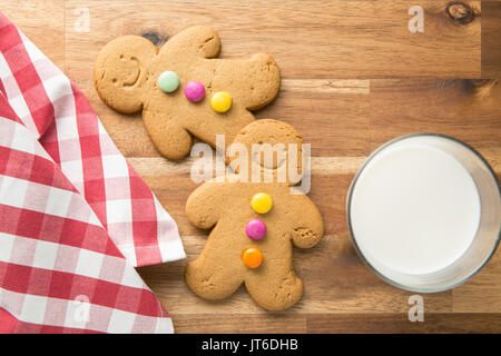 Sweet gingerbread men and glass of milk. Xmas gingerbread on wooden table. Stock Photo