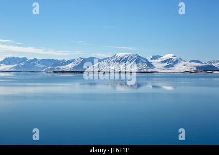 Snow covered mountains reflected in calm sea. Taken in June, Andoyane Islands, Northwest Spitsbergen, Svalbard, Norway Stock Photo
