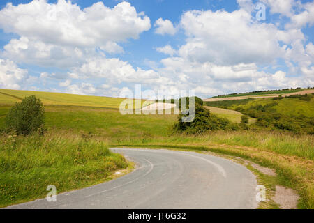 a curving road going into a green valley with grazing pasture hills and hedgerows under a blue summer sky in the yorkshire wolds Stock Photo
