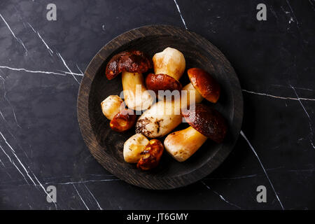 Raw wild Porcini mushrooms on wooden plate on dark marble table background Stock Photo