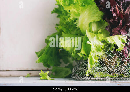 Fresh green and purple leaf salad in basket over old blue white wooden kitchen table. Rustic style, day light. Stock Photo