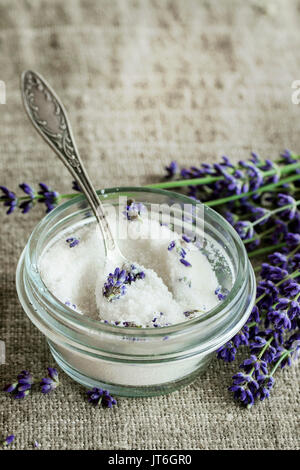 White sugar in glass jars flavored with lavender flowers, standing with tea spoon on table with sackcloth. Rustic style, day light Stock Photo