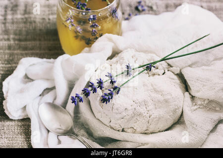 Fresh cooking homemade cottage cheese in gauze textile with lavender flowers and honey over sackcloth background. Rustic style, day light Stock Photo