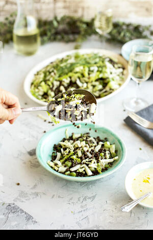 Black Lentil Green Veggie Salad served with Feta Mint Vinaigrette and white wine. Photographed on a grey plaster background. Stock Photo
