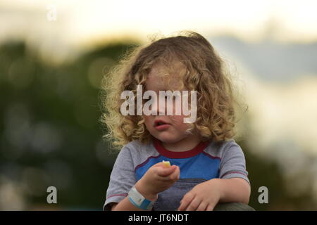 A curly-haired girl eating outside. Stock Photo