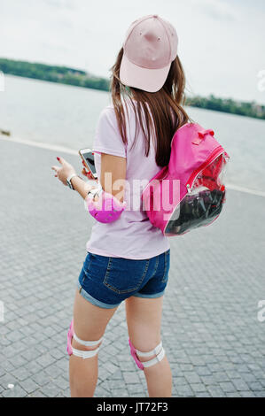 Portrait of a fantastic young woman roller skating with her phone in her hands in the park next to the lake. Stock Photo