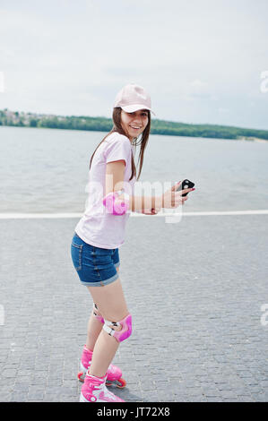 Portrait of a fantastic young woman roller skating with her phone in her hands in the park next to the lake. Stock Photo