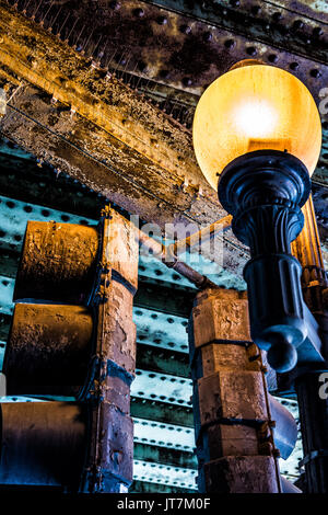 Closeup of illuminated lantern under railroad tracks bridge in Washington DC with grunge metal rust Stock Photo