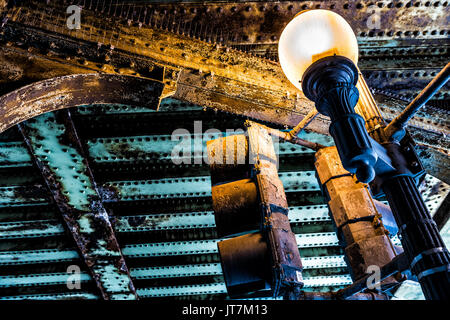 Closeup of illuminated lantern under railroad tracks bridge in Washington DC with grunge metal rust Stock Photo