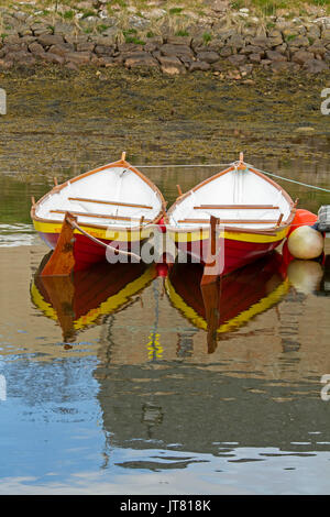 Two brightly coloured red, white, and yellow rowing boats / dinghies side by side & reflected in calm blue water of harbour at Helmsdale, Scotland Stock Photo