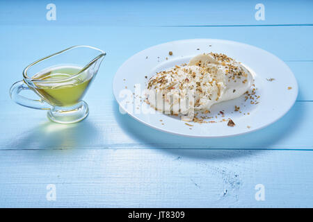 sliced mozzarella cheese served on white plate covered with provencal herbs with olive oil in glass jar on blue kitchen desk. low angle shot Stock Photo