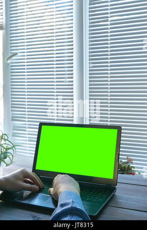 man working from home. mans hands in blue shirt typing on a laptop with green screen. copy space isolated cutout for your presentation. closed blinds  Stock Photo