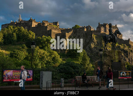 Edinburgh, Scotland, UK, August 7th 2017.  View of Edinburgh Castle from Princes Street, with Fringe festival posters on railings and pedestrians in Summer evening light Stock Photo